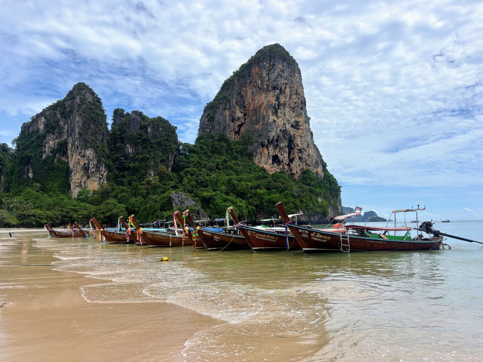 Longtail boats on Railay Beach in Krabi with limestone cliffs in the background