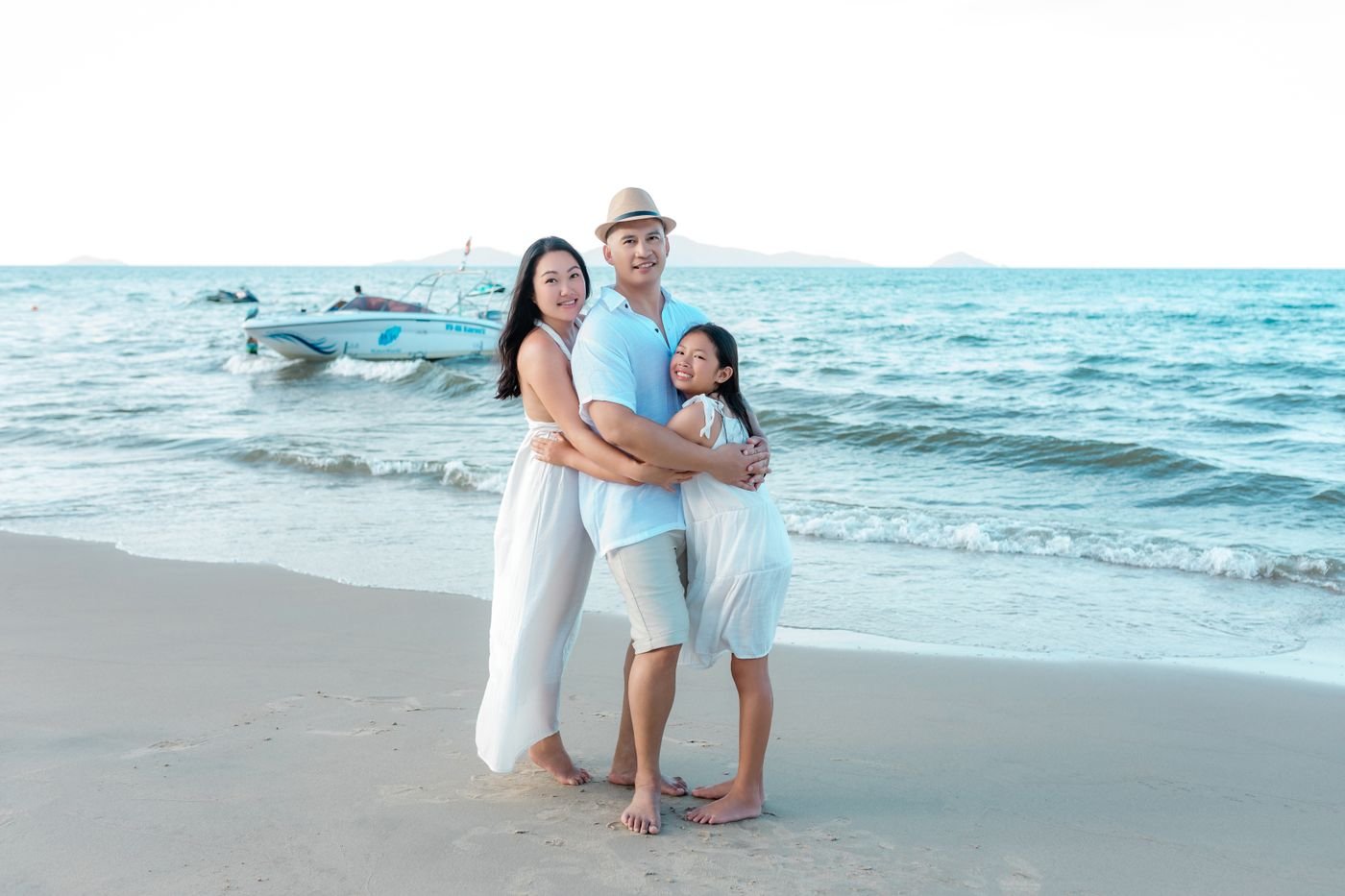 Family on the sand at An Bang beach in Hoi An, with waves and boats behind them