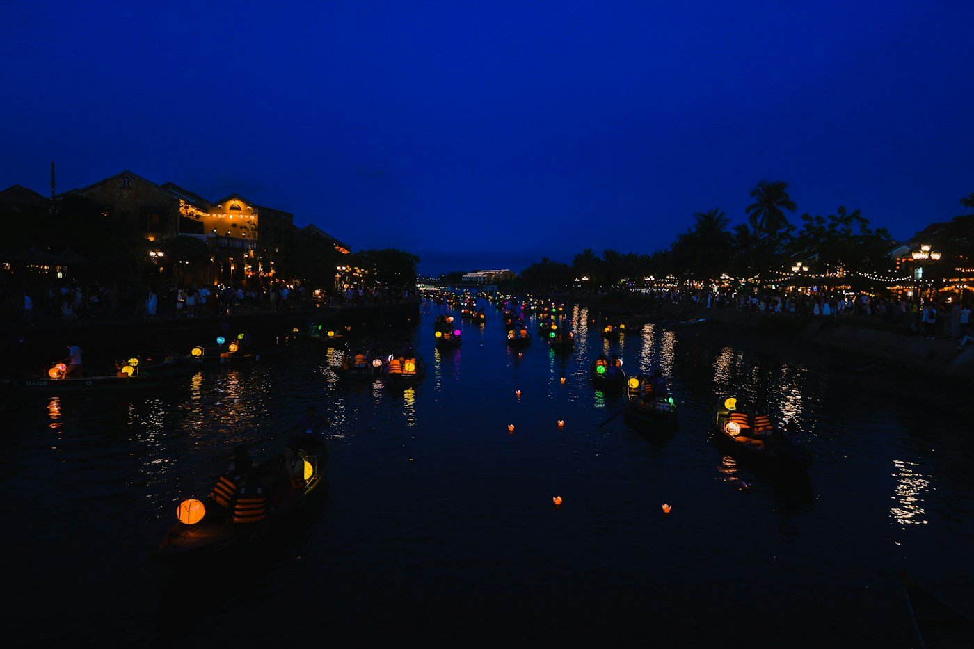 Lantern-lit boats and small floating candle lanterns on the river in Hoi An at dusk
